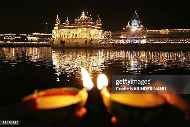 Indian Sikh devotees hold 'diyas' as they offer prayers in front of the illuminated Golden Temple on the eve of the festival of Bandi Chhor Divas in...