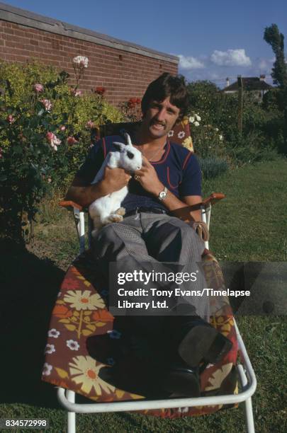 British soccer player David Johnson holds a rabbit, while laying down on a deckchair, July 1974.