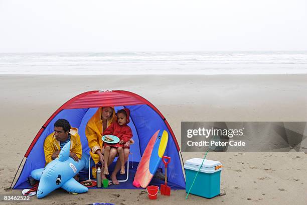 family on beach in the rain - teleurstelling stockfoto's en -beelden