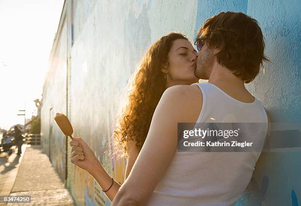 kissing couple leaning against wall - pecking stock-fotos und bilder