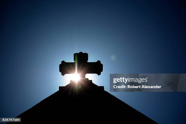 The morning sun rises behind a stone cross atop The Cathedral Basilica of St. Francis of Assisi, commonly known as Saint Francis Cathedral, in Santa...