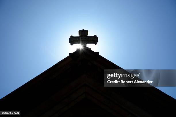 The morning sun rises behind a stone cross atop The Cathedral Basilica of St. Francis of Assisi, commonly known as Saint Francis Cathedral, in Santa...