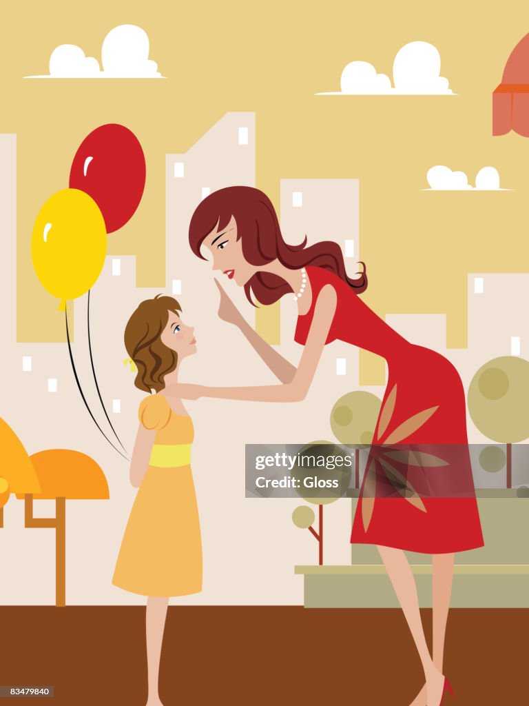 Side view of woman talking to her daughter who is holding balloons behind her back