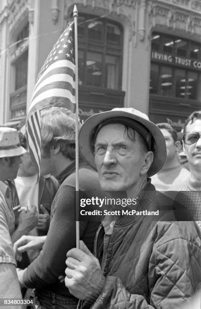 Downtown Manhattan May 1970: An older war veteran stands with an American Flag in hand, and protests along side construction workers, and other...