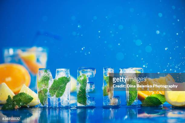 ice cube lettering with frozen mint leaves, lemon slices and oranges on a blue background with water splashes. text says melt. - ice alphabet stock pictures, royalty-free photos & images