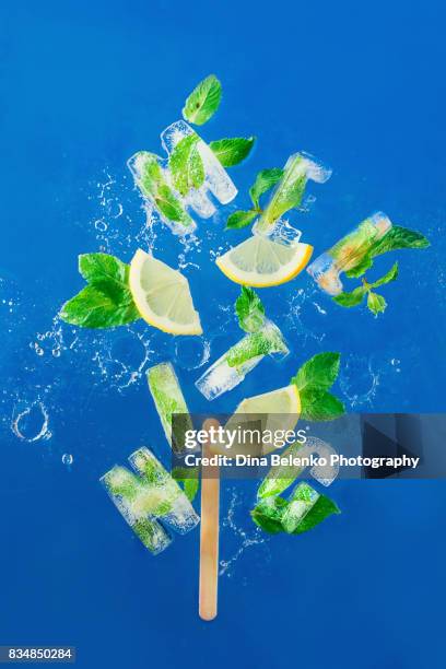 ice cube lettering with frozen mint leaves, lemon slices and oranges on a blue background with water splashes. text says melting. - ice alphabet stock pictures, royalty-free photos & images