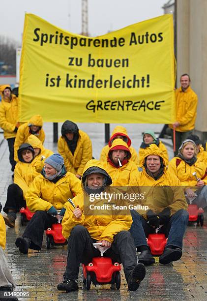 Greenpeace activists ride mini children's plastic cars in front of a banner that reads: "Building Low Fuel Consumption Cars Is Child's Play!" to...