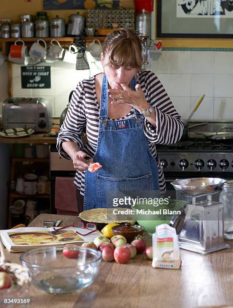 woman licks finger whilst cooking in kitchen - women licking women stock-fotos und bilder