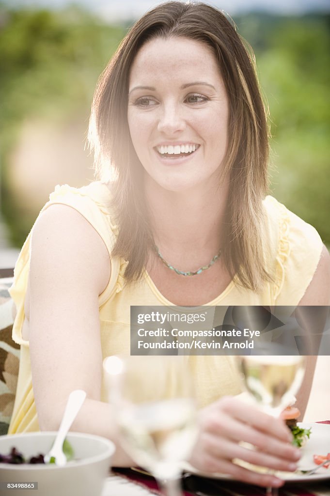 Woman eating dinner outdoors, smiling.