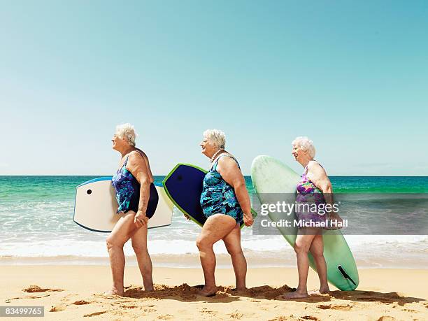 three mature women on beach with surfboards - old woman in swimsuit stock-fotos und bilder