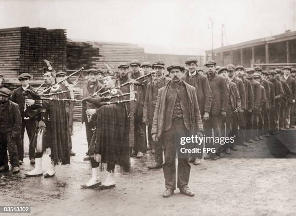 Group of shipyard workers, who have volunteered for military service, are led by pipers from their yard to a parade drill training session, Belfast,...