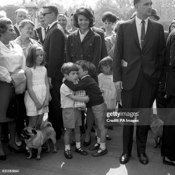 John Kennedy, son of the late American President John F Kennedy, clutches a loaf to his chest and listens as his cousin Anthony Radziwill takes him...