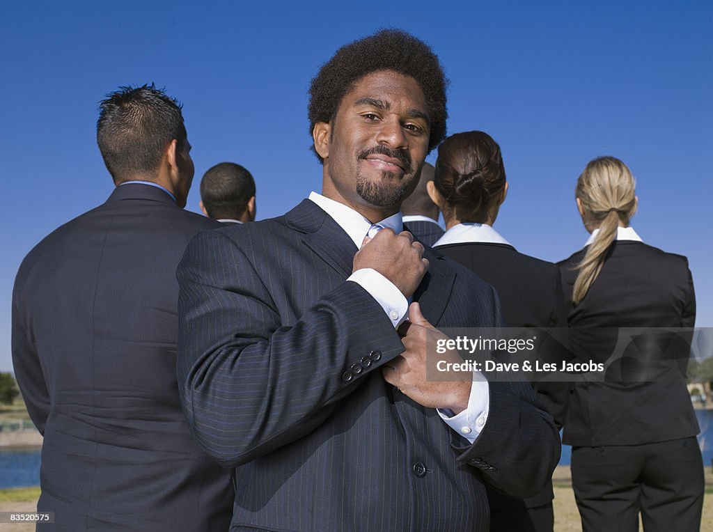 African businessman adjusting tie behind co-workers