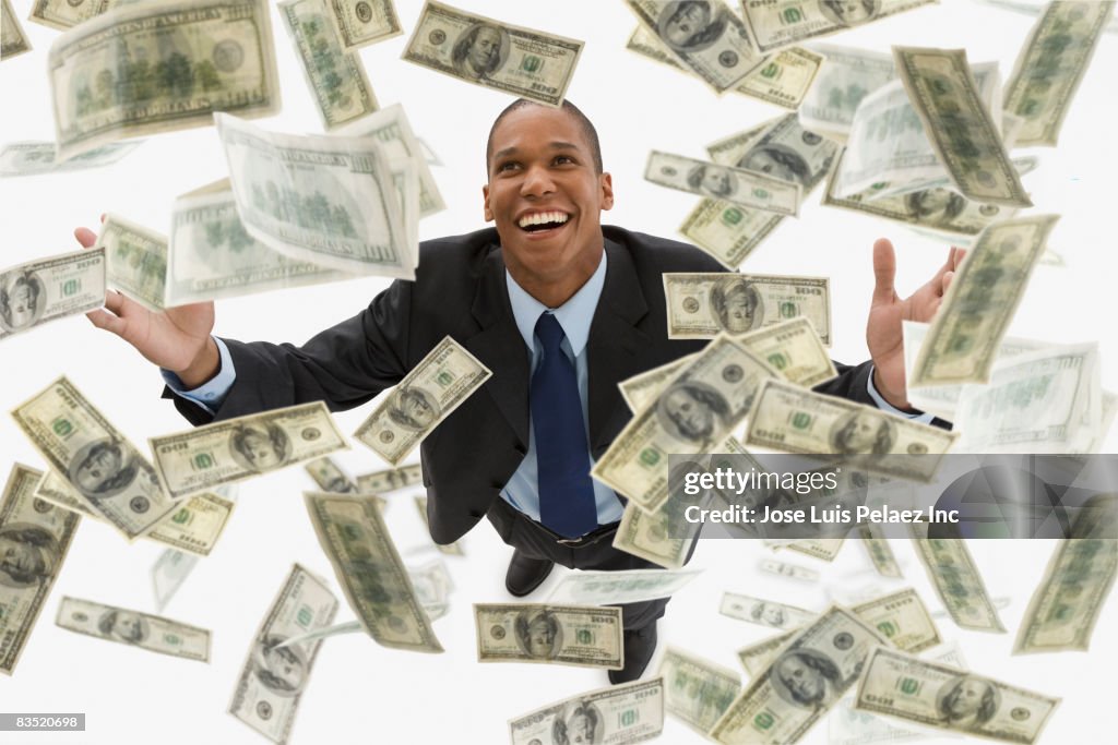Mixed race businessman catching falling 100 dollar bills