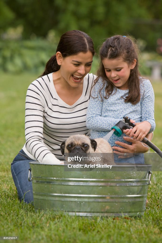 Hispanic mother and daughter washing dog