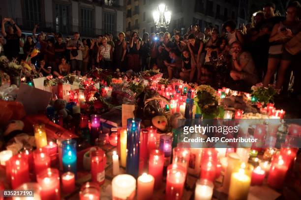 People stand next to flowers, candles and other items set up on the Las Ramblas boulevard in Barcelona as they pay tribute to the victims of the...