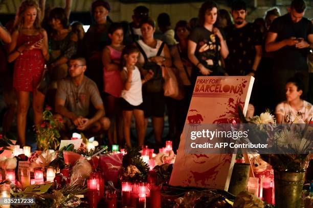 People stand next to flowers, candles and other items set up on the Las Ramblas boulevard in Barcelona as they pay tribute to the victims of the...