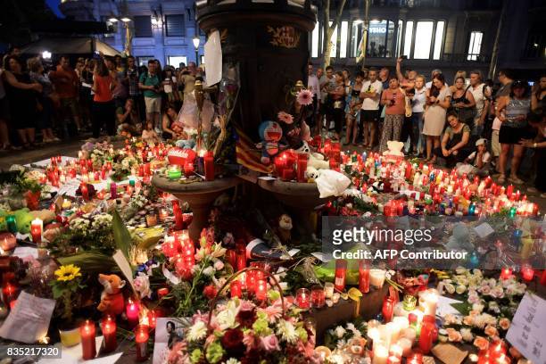 People stand next to flowers, candles and other items set up on the Las Ramblas boulevard in Barcelona as they pay tribute to the victims of the...