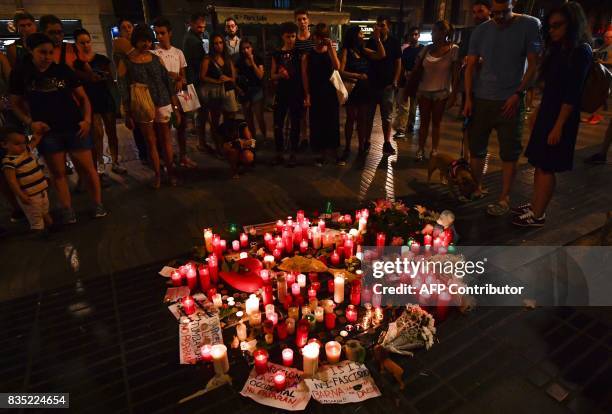 People stand next to flowers, candles and other items set up on the Las Ramblas boulevard in Barcelona as they pay tribute to the victims of the...