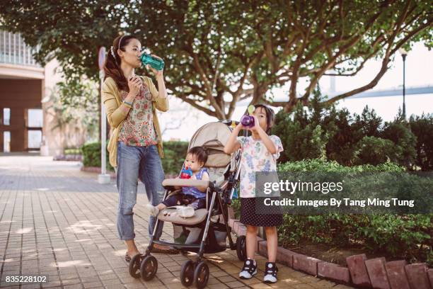 lovely little girl and her baby sister taking a rest drinking water with their pretty young mom at the promenade. - floral pattern pants stockfoto's en -beelden