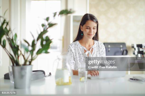 junge frau, die in ihrem büro arbeitet - wasser trinken büro stock-fotos und bilder