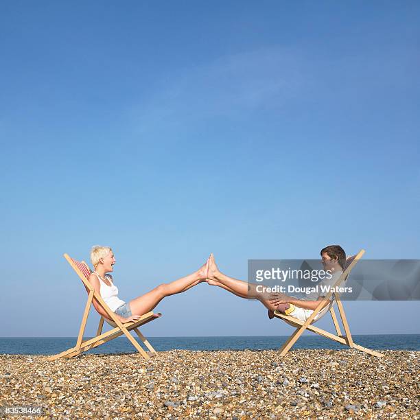 couple sitting on deck chairs with feet together. - female soles stock-fotos und bilder