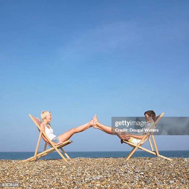 couple sitting on deck chairs with feet together. - soles pose stockfoto's en -beelden