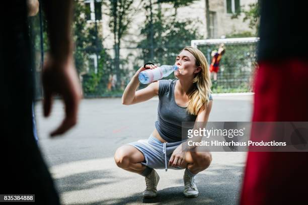 young woman taking break from basketball game to drink water - refreshment bottle stock pictures, royalty-free photos & images