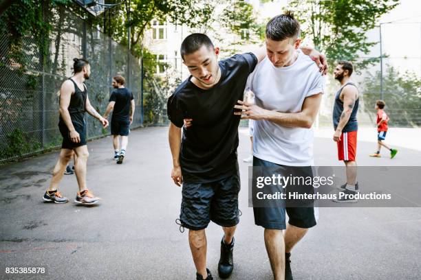 player assisting his injured teammate during urban basketball game. - unfall konzepte stock-fotos und bilder