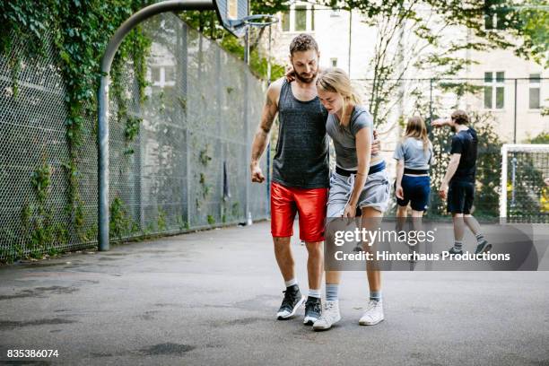 injured basketball player being assisted by her teammate - young man holding basketball stockfoto's en -beelden