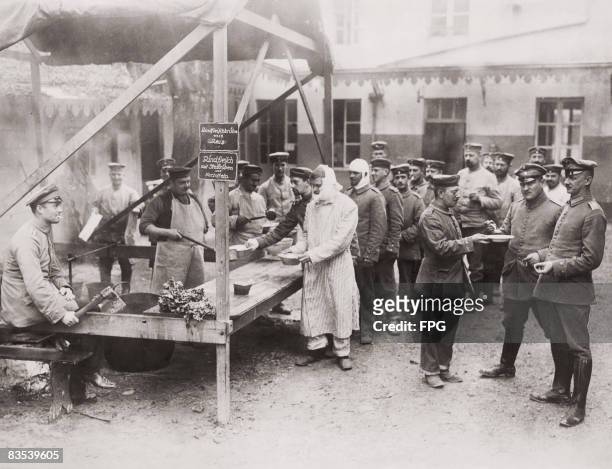Patients queue for food at a German field hospital near the front during the Meuse-Argonne Offensive in north-eastern France, 1918. Beef broth with...