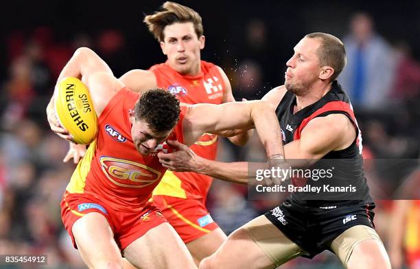 Suns player Pearce Hanley is pressured by the defence of James Kelly of the Bombers during the round 22 AFL match between the Gold Coast Suns and the...