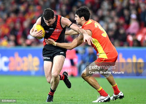 Conor McKenna of the Bombers is pressured by the defence of Matt Rosa of the Suns during the round 22 AFL match between the Gold Coast Suns and the...