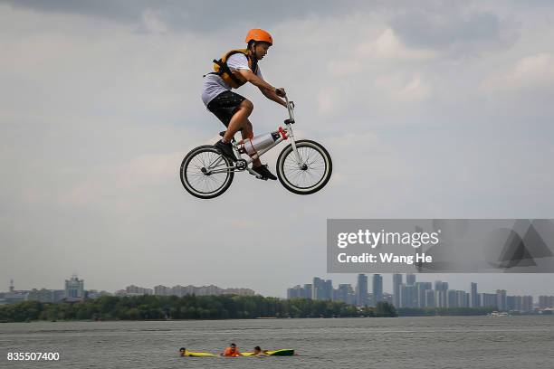 An extreme cycling enthusiast performs a stunt with a bicycle before falling into the East Lake on August 19, 2017 in Wuhan, Hubei province, China....