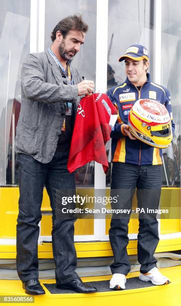Eric Cantona signs an old Manchester United replica shirt for Renault's Fernando Alonso during a photocall prior to the British Grand Prix at...