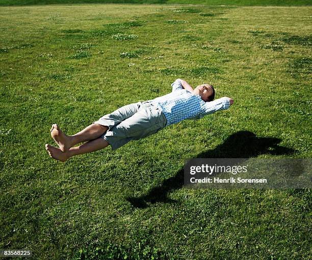 man realxing floating above the grass - levitation stock-fotos und bilder