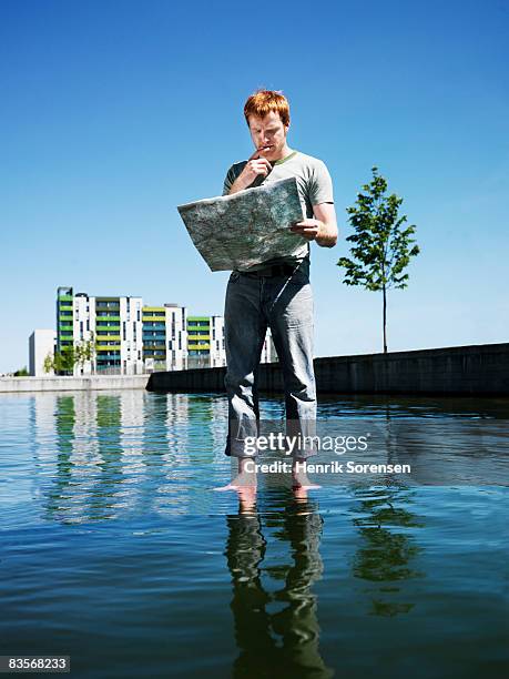 man standing on the water looking at a roadmap  - ankle deep in water fotografías e imágenes de stock