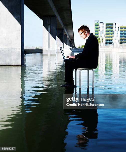 man sitting on the water working at his laptop - ankle deep in water fotografías e imágenes de stock