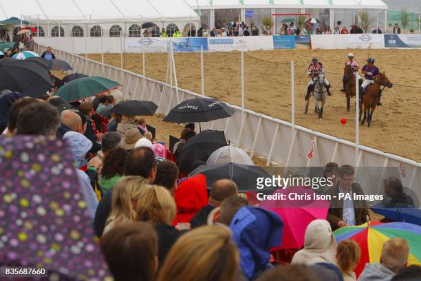 Sparse crowd watches the action during the British Beach Polo Championships from under raincoats and umbrellas at the exclusive Sandbanks area of...