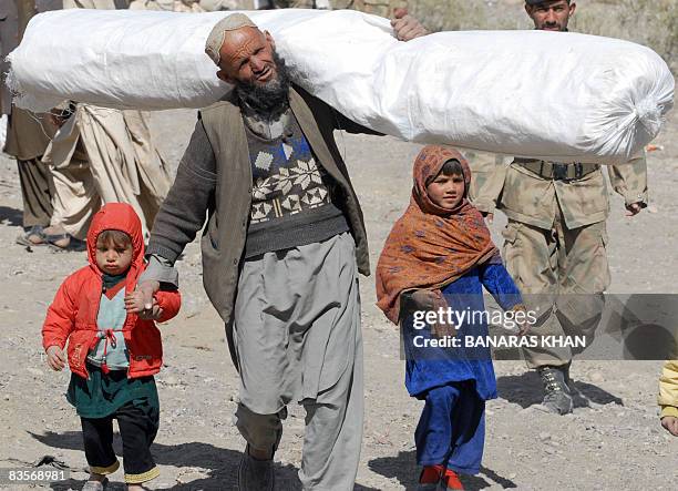 Pakistani earthquake survivor walks with his children as he carries a tent distributed by the army at a hilly area of Killy Kach, one of about eight...