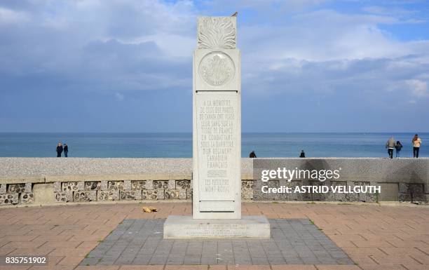 This photo taken on October 9, 2016 in Dieppe shows people walking on the beach next to a memorial dedicated to Canadian soldiers during the WWII...