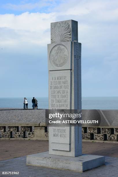 This photo taken on October 9, 2016 in Dieppe shows people walking on the beach next to a memorial dedicated to Canadian soldiers during the WWII...