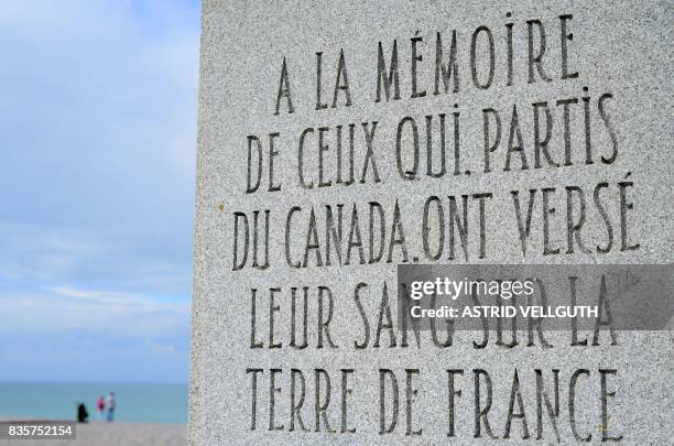 This photo taken on October 9, 2016 in Dieppe shows people standing on a beach next to part of a memorial reading 'In memory of those who left...