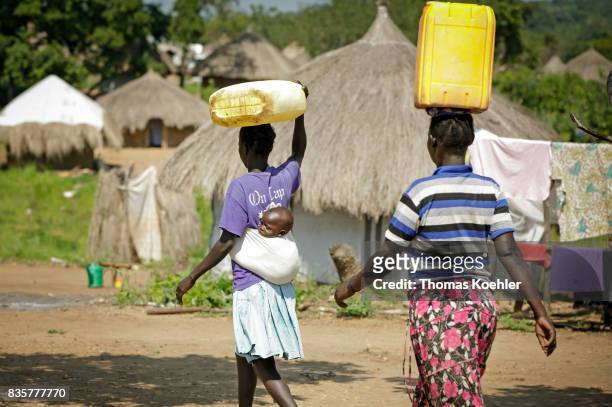Young women transport canisters with water on their head. One of them is carrying a child in a handkerchief on her back. Daily life at the Rhino...