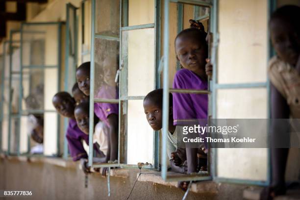 Students are looking out of an open window of a school at Rhino Refugee Camp Settlement in northern Uganda. Here, children of local people and...