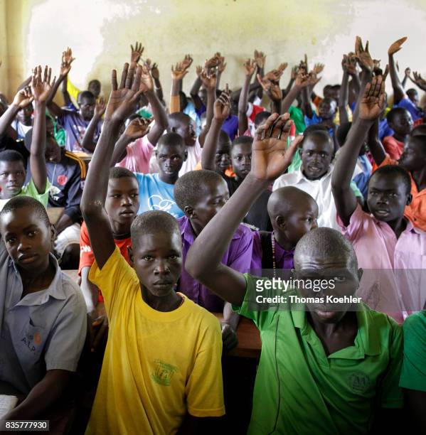 Group of students who raise their hands in a school at the Rhino Refugee Camp Settlement in northern Uganda. Here, children of local people and...