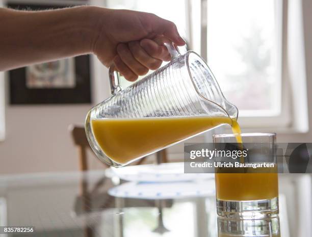 Vitamin C - Allroundgenie in terms of human health. The photo shows a hand with carafe during filling of orange juice into a glas.