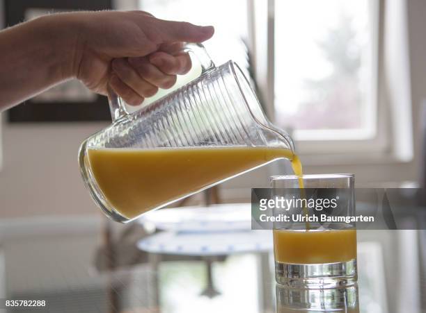 Vitamin C - Allroundgenie in terms of human health. The photo shows a hand with carafe during filling of orange juice into a glas.