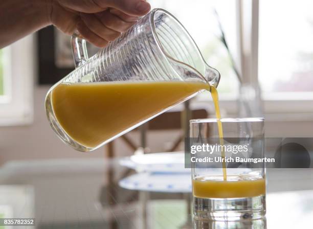 Vitamin C - Allroundgenie in terms of human health. The photo shows a hand with carafe during filling of orange juice into a glas.