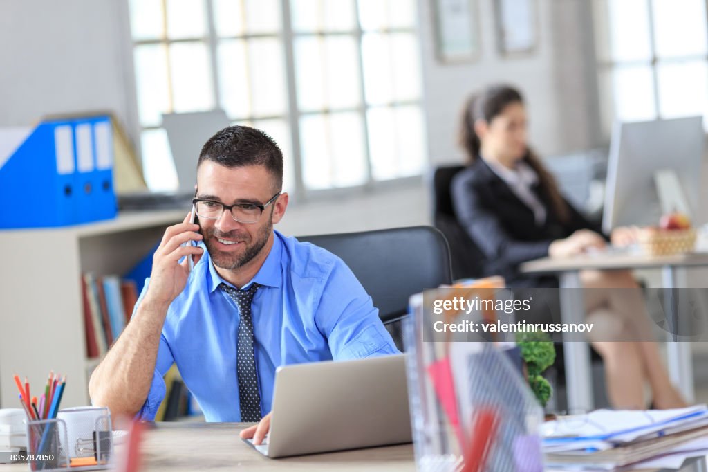 Smiling white collar worker using laptop and smart phone